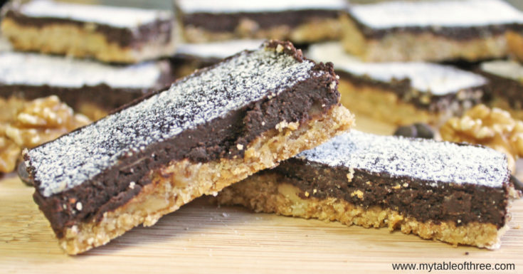 A close up photo of two Chocolate Walnut Bars stacked on one another with more cookies in the background.