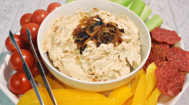 A bowl of caramelized onion dip on a platter with veggies for dipping.
