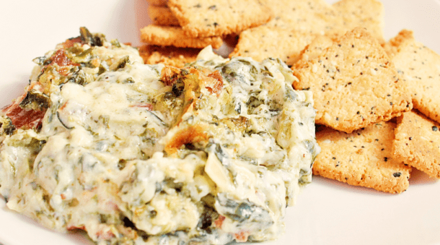 A serving of Spinach Artichoke dip with a side of crackers on a white plate.