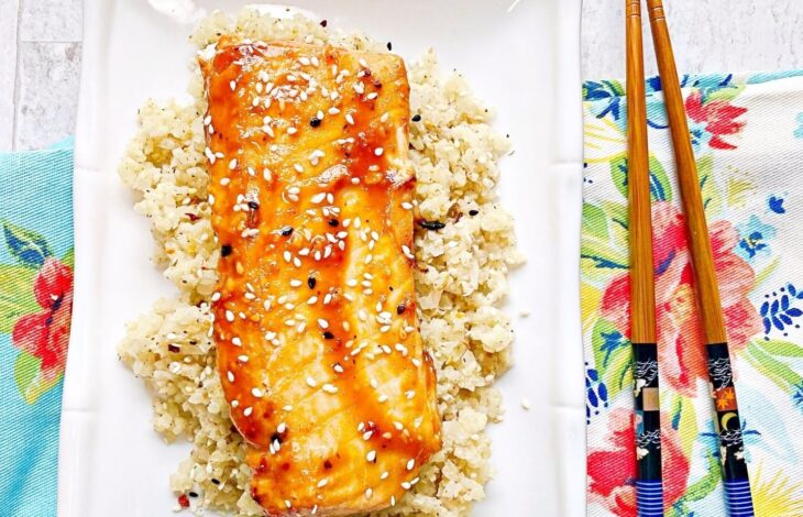 A plate of cauliflower rice with a whole piece of salmon laying on top. Chopsticks on the side.