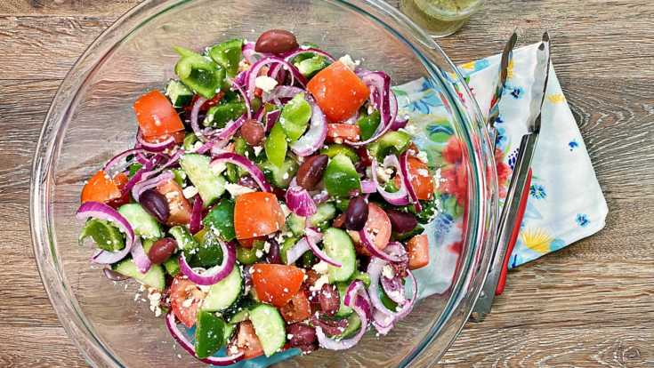 A large bowls of Greek Salad and serving tongs.