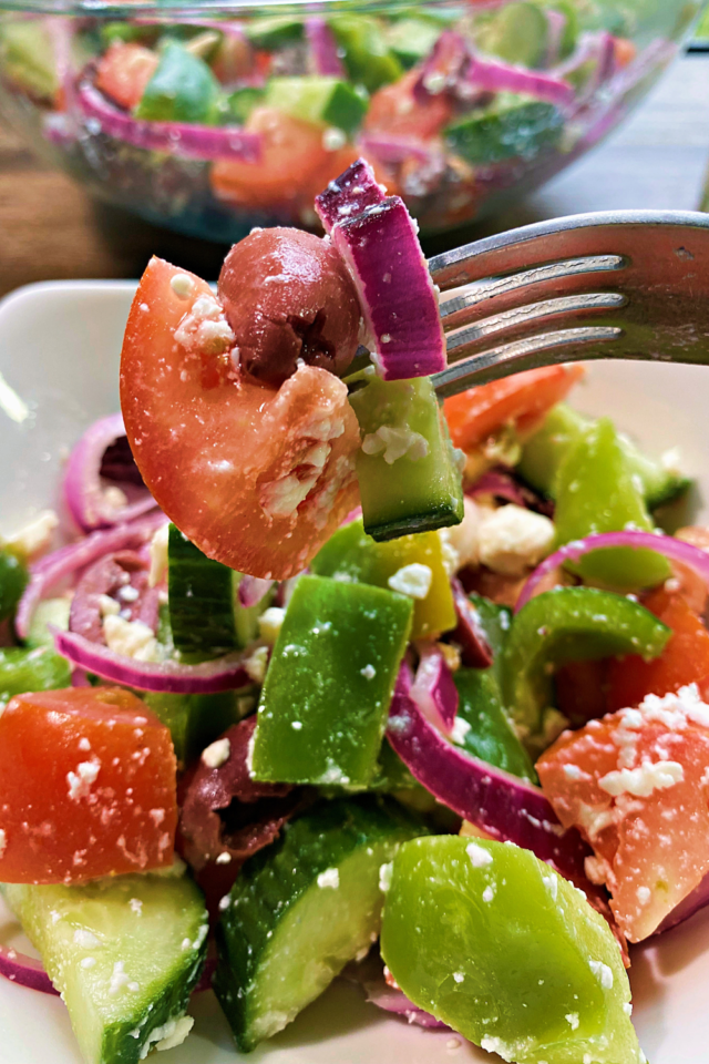 A close up photo of the greek salad. A bit of salad on a fork. 