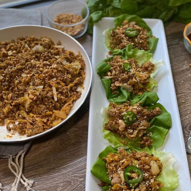 A skillet of lettuce wrap filling and a white plate with some lettuce wraps on it for serving.