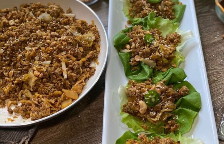 A skillet of lettuce wrap filling and a white plate with some lettuce wraps on it for serving.