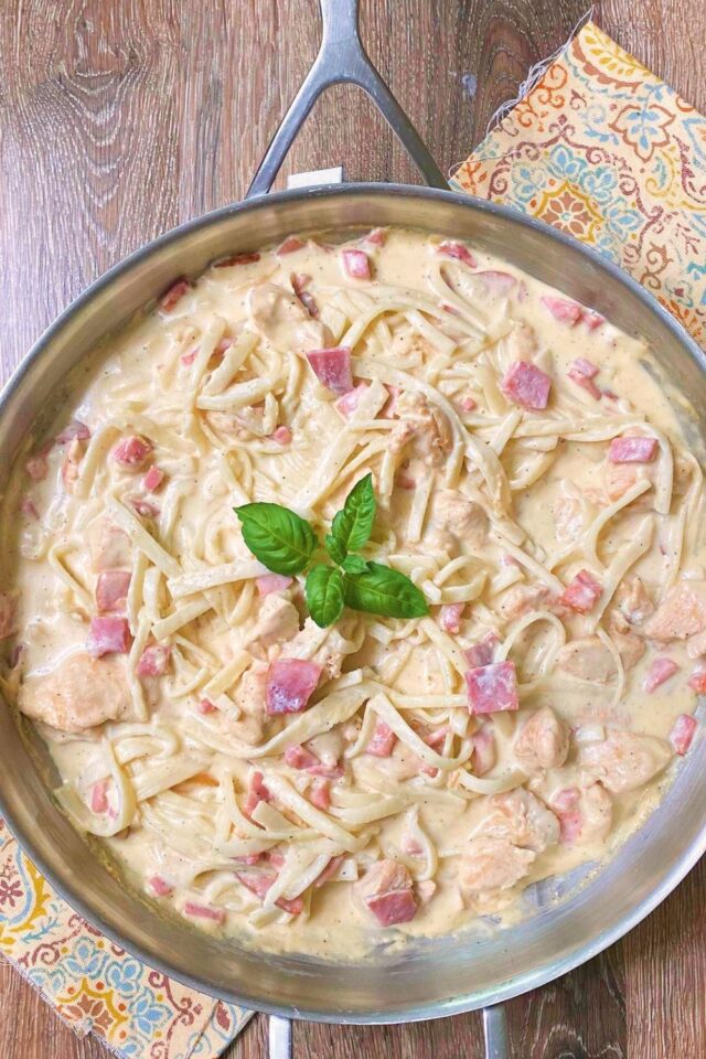 A top down look at a large silver skillet full of ham and chicken pasta.