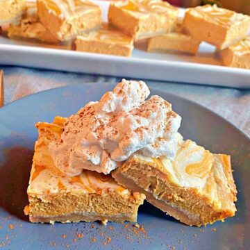 Two pumpkin bars on a plate topped with whipped cream.