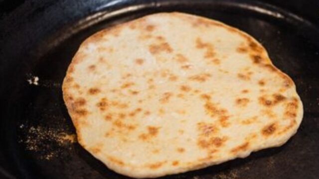 A naan bread after it has been flipped and is browned on top
