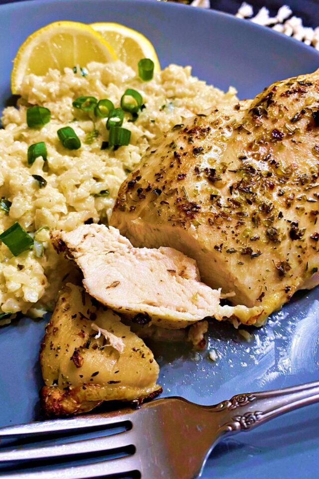 A sliced chicken breast with a fork lying on the right side and cauliflower rice behind it. 