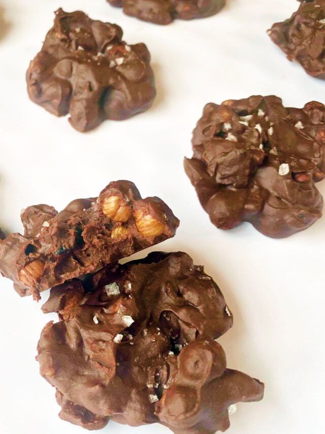 Nut clusters setting on a white baking may with a couple stacked on one another and one is displaying the center of the candy. 