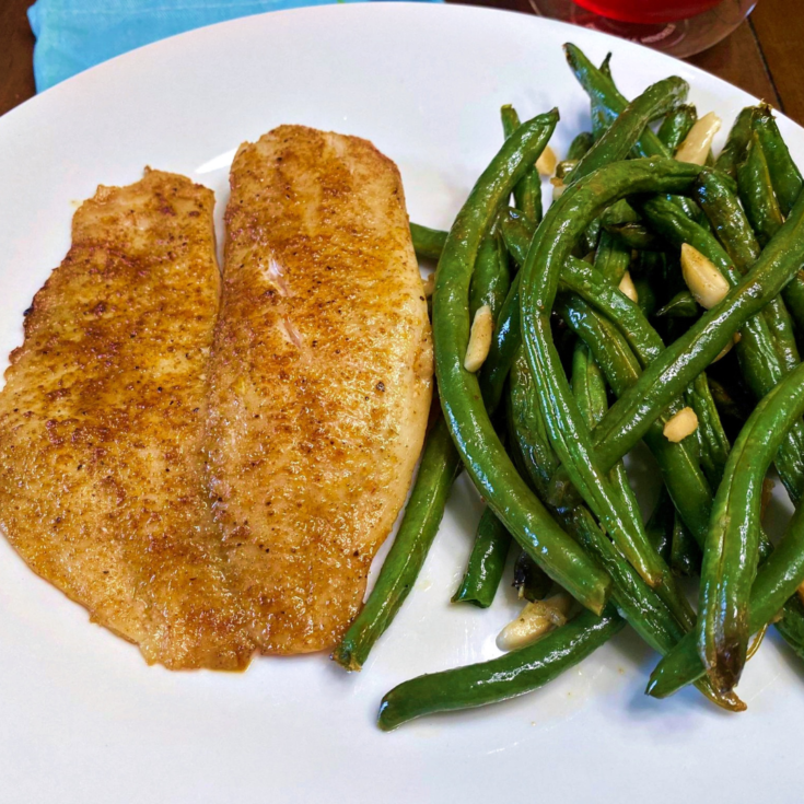 A Cajun spiced fillet of fish plated with long garlic green beans.