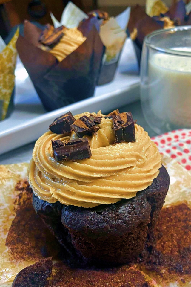 A chocolate cupcake unwrapped sitting in front of a platter of more cupcakes. 