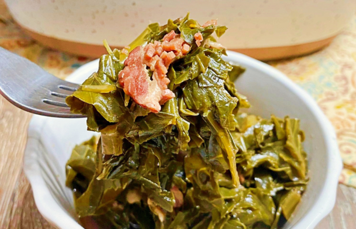 A fork holding of a bite of collard greens with a piece of bacon in the middle of collards.