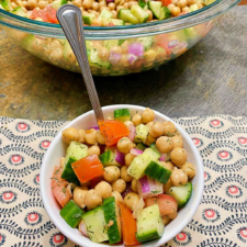 A small bowl of chickpea salad with a spoon stuck into the peas.