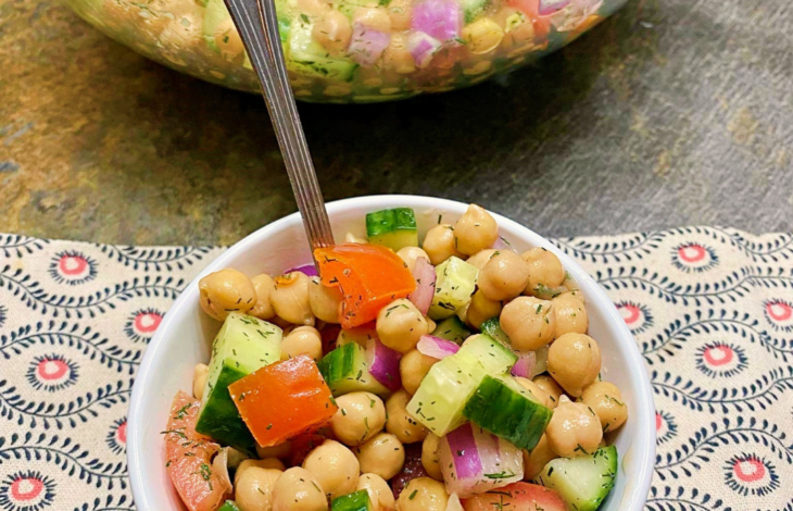 A small bowl of chickpea salad with a spoon stuck into the peas.