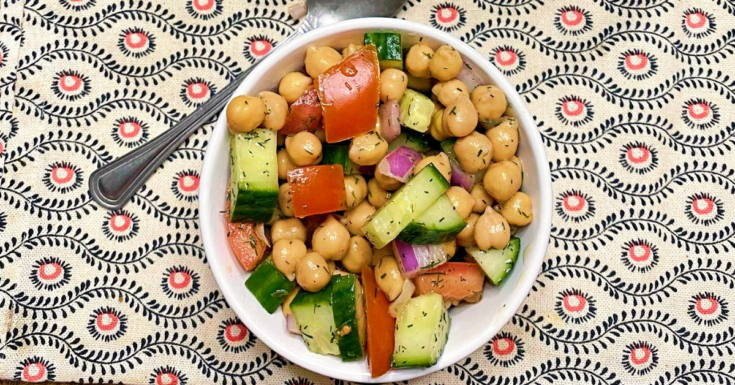 A small white bowl of chickpea salad with a silver spoon to the top left corner.