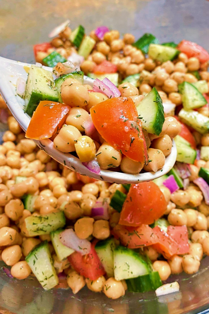 A large spoon full of the chickpea salad held over the clear serving bowl.