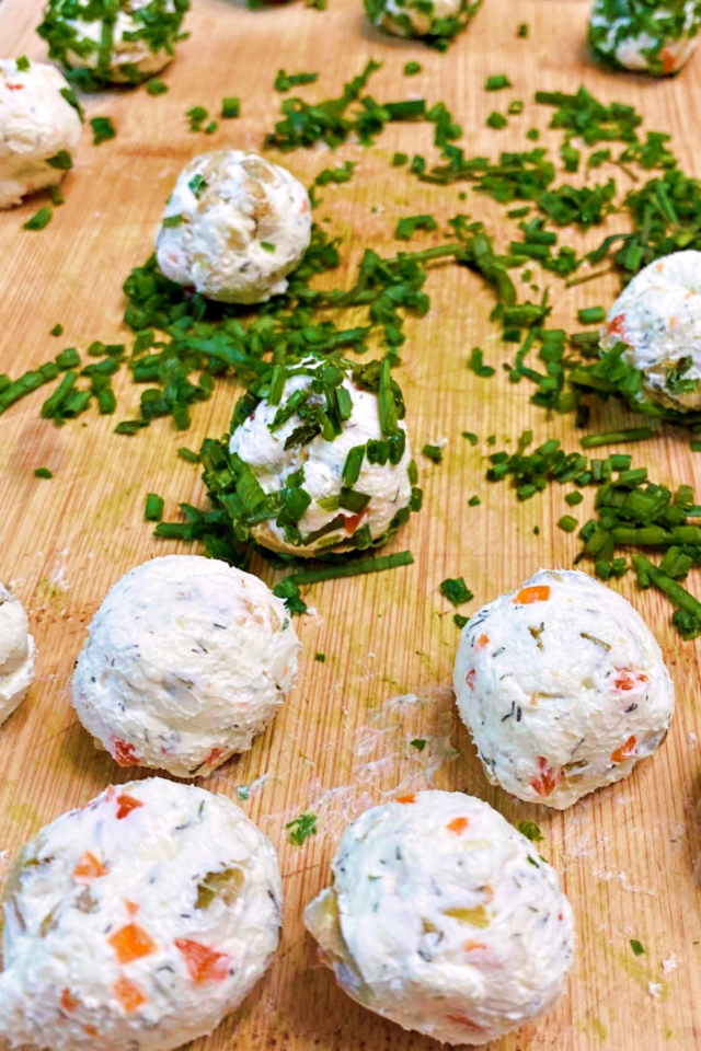 A cutting board with chopped chives and olive feta mini cheese balls on it. 