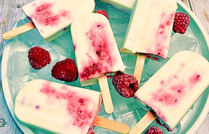 An icy plate of Raspberry Cheesecake Popsicles surrounded by fresh red raspberries.