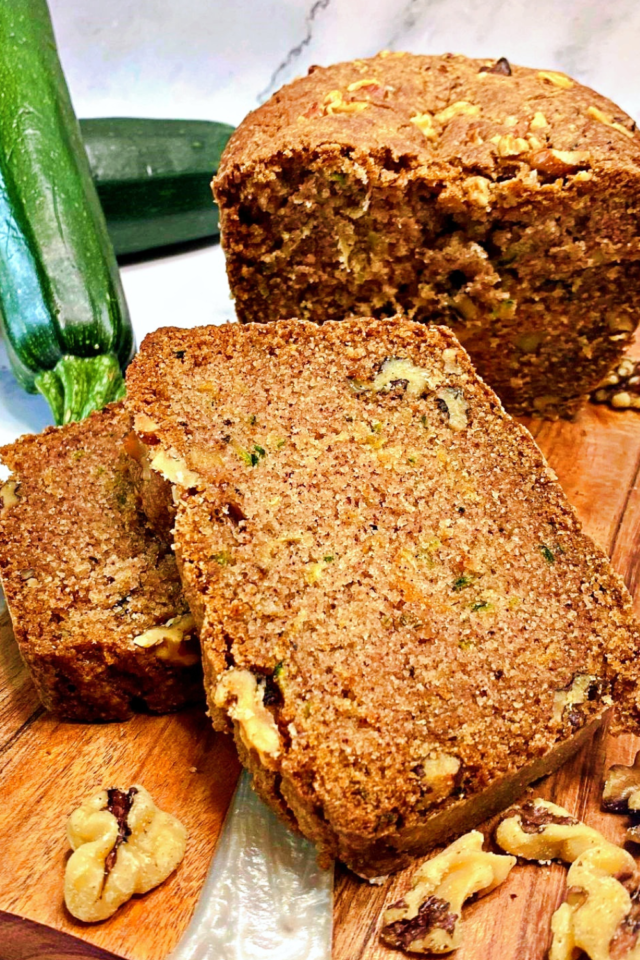 Two slices of zucchini bread stacked on top of one another with fresh zucchini in the background.
