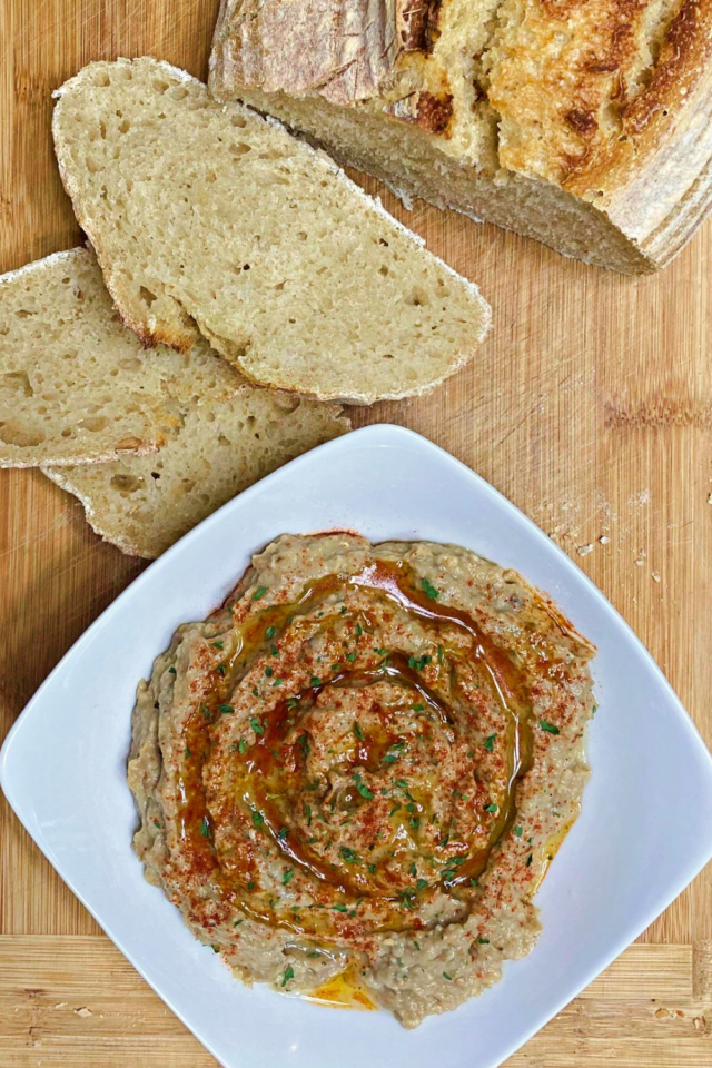 A top down photo of the Roasted Eggplant Dip in a white serving bowls with a sliced loaf of sourdough bread.