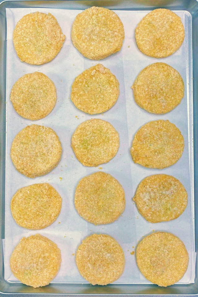 A vertical photo of a tray of breaded yellow squash slices.