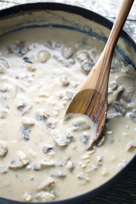 A top down photo of a sauce pan full of cream of mushroom show and a wooden spoon in the soup.