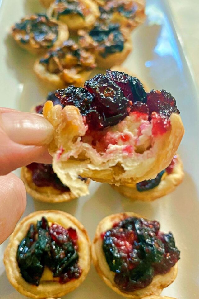 A hand holding a mini tart with a bite out of it to expose the inside.