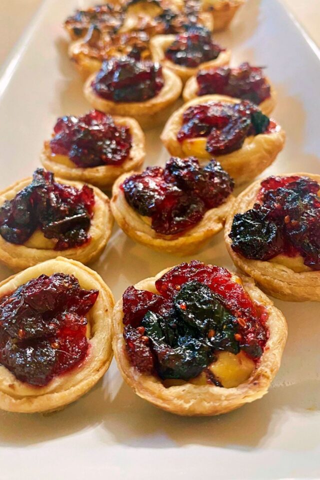 Several Mini Cranberry and Goat Cheese Tarts lined up on a white serving tray.